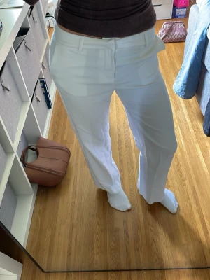 Vita raka kostymbyxor midwaist - Säljer ett par vita kostymbyxor med rak passform och pressveck. Byxorna har hällor för skärp och diskreta sidofickor. Perfekta för en clean och stilren look