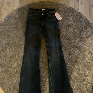 Bootcut jeans från Nelly, mörkblå - Mörkblå bootcut jeans från Nelly med snygga kontrastsömmar och broderade bakfickor. Jeansen har låg midja, klassisk femficksdesign och stängs med dubbla knappar och dragkedja. Jeansen är i Storlek 38 dock lite mindre även för mig som vanligtvis har 38 och har dessa byxor sedan tidigare i 38, så passar nog även en strl 36. 