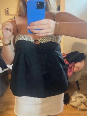 Svart topp med strass från Zara - Säljer en svart topp från Zara med tunna axelband och glittriga strassdetaljer över bysten. Toppen har en luftig passform och är perfekt för dig som vill sticka ut lite extra. Supersnygg att styla med kjol eller jeans!