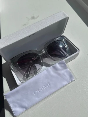 Transparenta solglasögon från Chimi - Säljer ett par stilrena solglasögon från Chimi med transparent båge och mörka glas. Kommer i originaletui och med putsduk. Snygg, modern design som passar till alla looks.