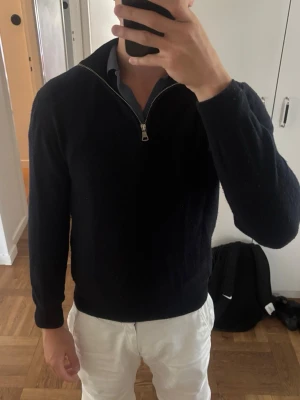 Mörkblå halvzip Kashmir-tröja Oscar Jacobson - Klassisk mörkblå tröja med halvzip och hög krage. Tröjan har lång ärm och är i kashmir, enkel design som passar till skjorta under. Perfekt för dig som gillar en clean och tidlös look.