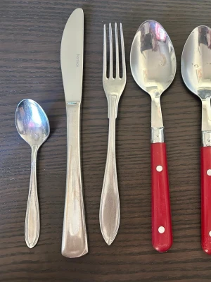 Blandade bestick - Bestickset om 8 delar. Besticken är i rostfritt stål. Gafflarna och skedarna har handtag i rött och blått.  Skick kan ses på bilder!!