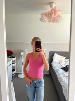 Rosa croppad linnetopp med korsade band - Säljer en rosa croppad linnetopp med smala axelband som korsas i ryggen. Toppen är ärmlös och har en slim passform som sitter snyggt mot kroppen. Är i träningsmaterial 