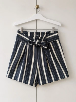 Randiga högmidjade shorts med knyt - Snygga högmidjade shorts med marinblå och vita ränder. Shortsen har ett brett midjeband med knyt i midjan och två fickor bak. Perfekta för sommarens alla äventyr och ger en fräsch look.
