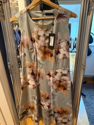 Blommig klänning från STOCKH LM - Snygg blommig klänning från STOCKH LM i ljusa toner med inslag av beige, lila och brunt. Klänningen är ärmlös, har rund halsringning och dragkedja i ryggen. Perfekt för sommarens alla tillfällen.
