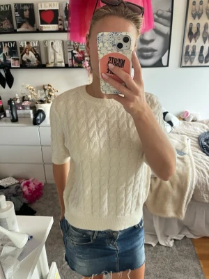Vit kabelstickad tröja kort ärm - Säljer en vit kabelstickad tröja med korta ärmar och rund hals. Tröjan har ribbade muddar vid ärmslut och nederkant, vilket ger en snygg och klassisk look. Perfekt att matcha med jeans eller kjol för en trendig outfit.
