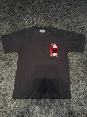Svart Casa Blanca t-shirt med tryck - Snygg svart t-shirt från Casa Blanca med stort grafiskt tryck i rött, vitt och svart på ryggen och mindre tryck på bröstet. Klassisk passform och rund hals. Perfekt för dig som vill sticka ut med en unik design.