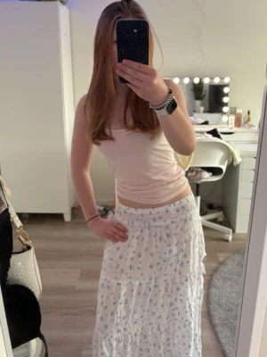 Vit långkjol med blå blommor - Söt långkjol med slits, liten sömsprett högst upp men går lätt att sy förhand. Storlek xs, älskar denna men säljer den pga sömmen..är för lat för att fixa själv. Helt ren och fin, inga fläckar. Från New Yorker. 
