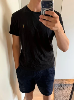 Svart t-shirt från Polo Ralph Lauren - Klassisk svart t-shirt från Polo Ralph Lauren med den ikoniska broderade loggan på bröstet. T-shirten har rund halsringning och korta ärmar. Tillverkad i mjuk bomull som känns skön mot huden. Perfekt basplagg till garderoben.