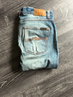 Nudie jeans 30/30 - Säljer ett par ljusblå jeans från Nudie Jeans med snygga slitningar. Hör av er vid frågor!