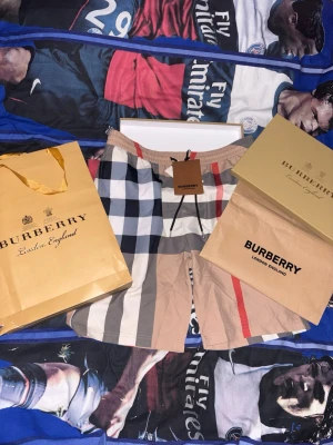Burberry shorts - Säljer ett par klassiska Burberry shorts med ikoniskt rutigt mönster i beige, svart, vitt och rött. Shortsen har elastisk midja och är tillverkade i mjuk bomull. Perfekta för sommaren och ger en clean och lyxig vibe. Storleken är i L men passar även M. Priset går alltid att diskuteras!