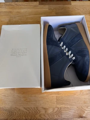 Maison Margiela gats  - Snygga mörkblå sneakers från Maison Margiela med ovandel i mocka och läder, vita skosnören och klassisk gummisula. Perfekt för dig som gillar stilrena och tidlösa sneakers med exklusiv känsla.