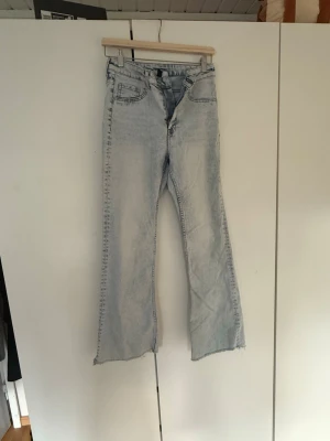 Ljusblå utsvängda jeans - Säljer ett par ljusblå jeans med utsvängda ben och råa kanter nertill. Jeansen har klassisk femficksdesign och hög midja. Perfekta för dig som gillar en avslappnad och trendig look.