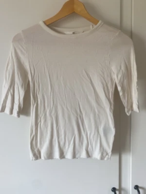 Vit topp från H&M med trekvartsärm - En enkel och stilren vit topp från H&M med rund halsringning och trekvartsärm. Tillverkad i mjuk bomull som känns skön mot huden. Perfekt att matcha med jeans eller kjol för en clean look.