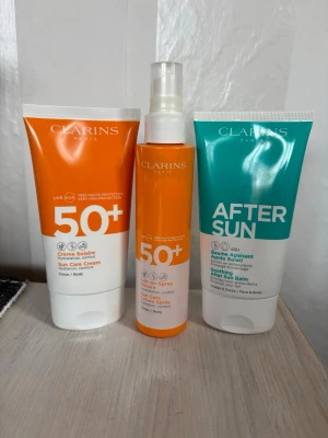 Clarins solskydd och after sun set - Set med två solskyddsprodukter SPF 50+ och en after sun från Clarins. Solkrämen och solsprayen har orange och vit design, after sun är turkos och vit. Passar både kropp och ansikte. Perfekt för soliga dagar och återfuktning efter sol.