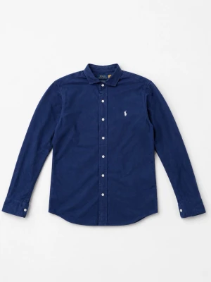 Mörkblå skjorta från Polo Ralph Lauren - Klassisk mörkblå skjorta från Polo Ralph Lauren med vit broderad logga på bröstet. Skjortan har långa ärmar, knappar framtill och en tidlös krage. Perfekt för en stilren look.