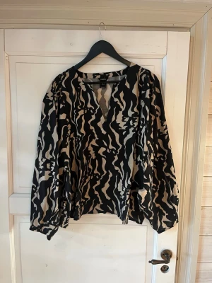 Mönstrad svartvit blus med v-ringning - Snygg långärmad blus med svart och beige abstrakt mönster och v-ringning.