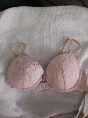 Ljusrosa push-up bh med spets - Söt ljusrosa push-up bh med vadderade kupor och fina spetsdetaljer framtill. Justerbara axelband och hakknäppning bak. Bh:n har en romantisk look med blommig spets och mjukt material för extra komfort.