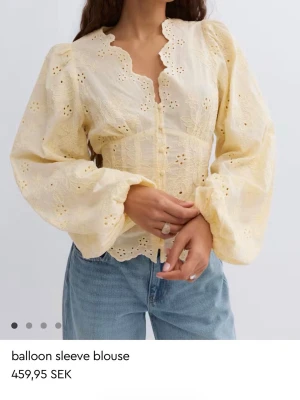 Gul blus med ballongärmar - Söt ljusgul blus med broderade detaljer och ballongärmar. Blusen har v-ringning med vågig kant, knäppning framtill och broderade blommor. Materialet ser ut att vara bomull eller en bomullsblandning. Perfekt för en trendig och feminin look.