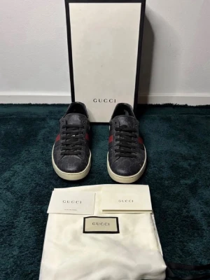 Gucci GG Supreme sneakers svart/röd - Snygga Gucci GG Supreme sneakers i svart med klassiska röda och mörkblå ränder på sidan. Skorna har låg profil, vit sula och är tillverkade i canvas med läderdetaljer. Perfekta för dig som vill ha en exklusiv och trendig look pris kan diskuteras vid snabb affär allt og tillkommer kvitto finns🫡