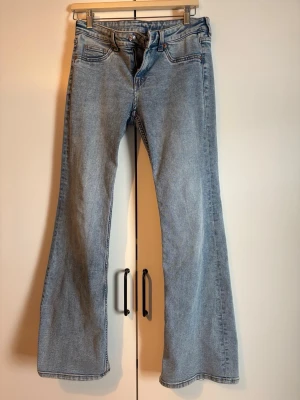 Ljusblå utsvängda jeans - Säljer ett par ljusblå jeans med utsvängda ben och klassisk femficksmodell. Jeansen har hög midja och är tillverkade i denim med en snygg tvätt. Perfekta för dig som gillar retrostil och vill ha ett par riktigt schyssta jeans i garderoben.