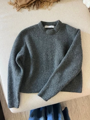 Mörkgrå stickad tröja från Bershka - Mysig mörkgrå stickad tröja från Bershka i storlek XS. Tröjan har en enkel, rak passform med rund halsringning och långa ärmar. Materialet är fluffigt och ger en avslappnad look, perfekt för kyliga dagar.