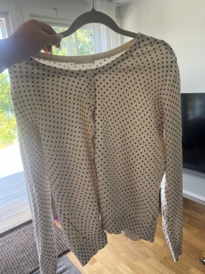 Prickig beige kofta från H&M - Söt beige kofta från H&M med små svarta prickar över hela plagget. Koftan har rund halsringning, knäppning framtill och långa ärmar. Perfekt för lager på lager och enkel att matcha med olika outfits.