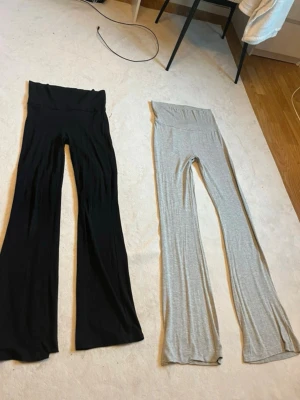 Två par utsvängda leggings - Säljer två par leggings med utsvängda ben, ett par i svart och ett par i ljusgrått. Båda har hög midja och är gjorda i mjukt, stretchigt material som sitter skönt på kroppen. Perfekta för en avslappnad och trendig look.