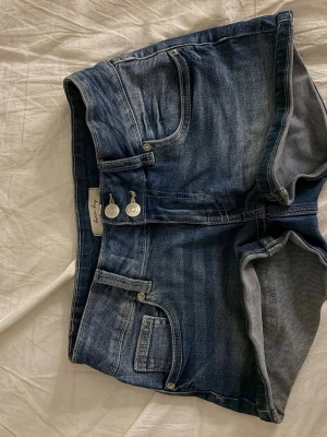 Mini Low waist shorts - Säljer ett par klassiska blå denimshorts från Denim Day i storlek 152. Shortsen har hög midja, två framfickor, två bakfickor och dubbla silverfärgade knappar framtill. Perfekta för sommaren och tillverkade i slitstark bomull.