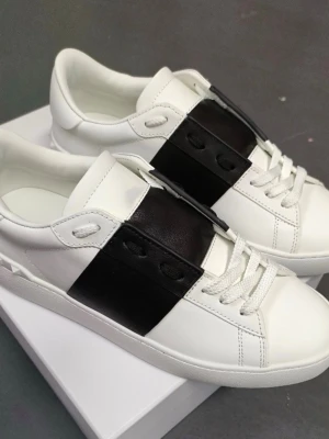 Vita sneakers med bred svart detalj - Stilrena vita sneakers med en bred svart läderdetalj över snörningen. Skorna har klassisk låg profil, vita snören och en vit sula. Perfekta för dig som gillar minimalistisk och modern design. Materialet är slätt läder och detaljerna ger ett exklusivt intryck.