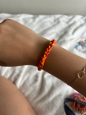 Färgglatt flätat vänskapsarmband - Säljer ett handgjort vänskapsarmband i flätad design med starka färger i rött, orange och gult. Armbandet är gjort av mjukt garn och justerbar enkelt runt handleden. Perfekt för dig som gillar färg och vill ha en personlig accessoar.💕
