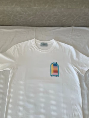 Vit Casa Blanca t-shirt med tryck - Säljer en vit t-shirt från Casa Blanca med ett färgglatt grafiskt tryck på bröstet. T-shirten har rund hals och korta ärmar. Perfekt för dig som gillar stilrena plagg med en twist.