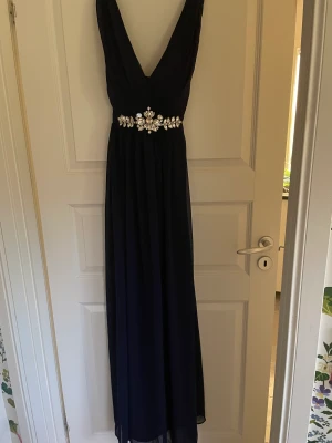 Marinblå balklänning med silversmycke - Oanvänd balklänning med silversmycke i storlek L (14 UK) Helt ny, bara provad.  Skulle jämföra med storlek 42.  Går bra för upphämtning i Borlänge. Frakt tillkommer om ni vill att jag skickar den