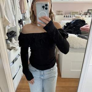 En svart långärmad Off-shoulder tröja med volang.