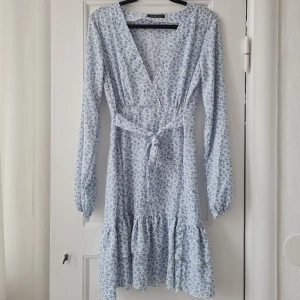 Sommarklänning - Klänning med vit botten och blåa blommor. Dragkedja finns i sidan och band på vardera sida som knyts fram eller bak. Använd 1 gång