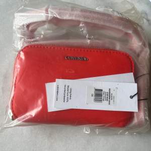 Säljer denna helt nya Calvin Klein pochette väska i korallröd färg. Helt ny med lapparna kvar. 