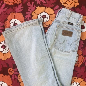 Wrangler jeans - ljusblå bootcutjeans från wrangler. Lågmidjade. Köpta second hand. Har några bleka fläckar men inget man tänker på när de är på, annars i gott skick! Storlek 26/32 enligt lapp men se mått. 100% bomull.  // mått // midja: 68 cm // längd utsida: 103 cm //