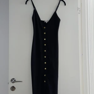 Svart klänning med guldknappar  - Aldrig använd, endast provad!  De tre nedersta knapparna går att öppna upp, resten är endast för dekoration!