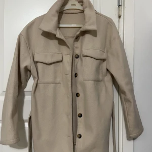 Höst jacka - En bekväm och vacker höstjacka i beige, ett bälte till jackan finns också. Storlek S men passar även M