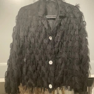 Festlig svart blus - Svart blus med vita knappar. Lappar saknas så osäker på märke och storlek men uppskattar den till en S/M. Går även att använda som en ”jacka” och piffar till vilken outfit som helst.