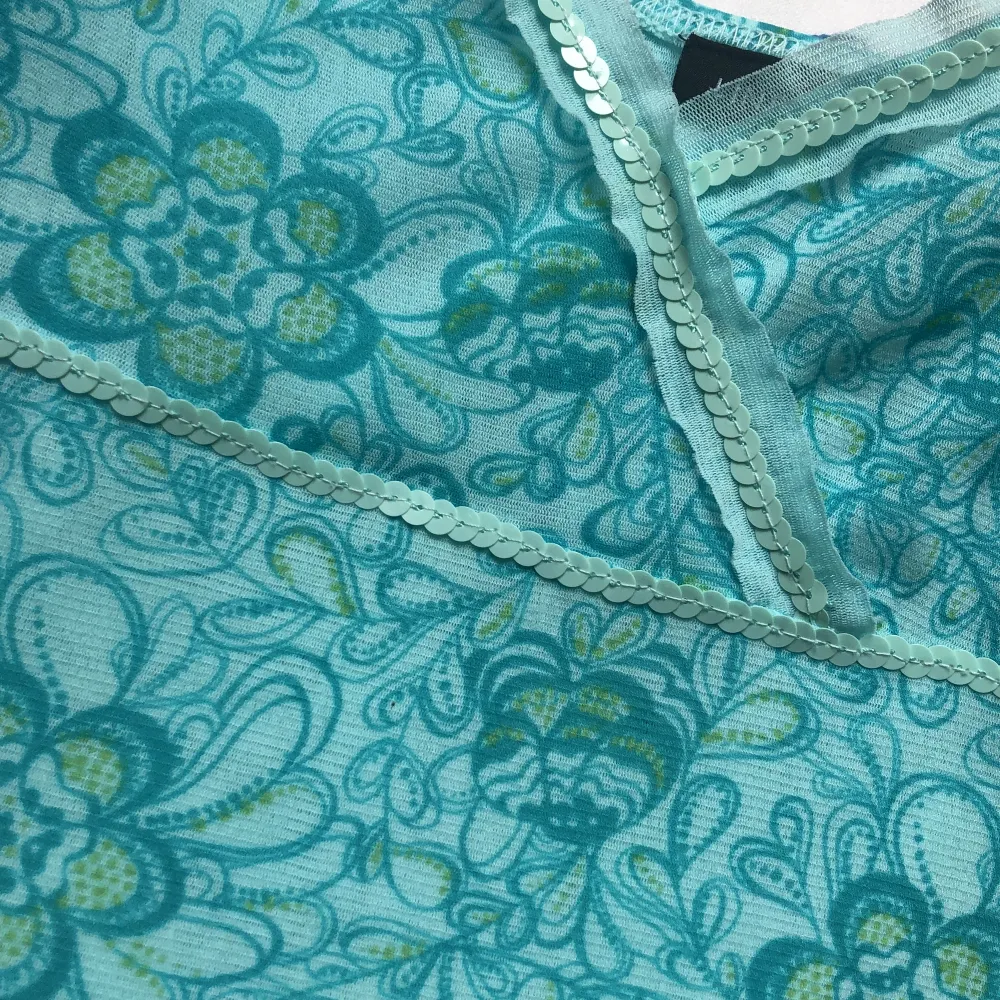 Ett blått/turkost linne med blommigt mönster och paljetter på, köpt på Lindex på cirka 90/2000-talet. Ungefär 72 cm långt. Finns lite lösa trådar och en paljett har ett hål i kanten. Har tvättat bort fläckarna!! Jag kan ta fler bilder om man vill🩷. Toppar.