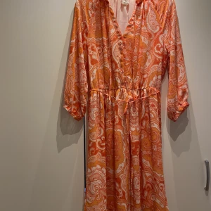 Klänning  - Bra skick, använd fåtal gånger. Tunt band som knyts runt midjan, ligger precis ovanför en resår som går runt midjan i klänningen. 