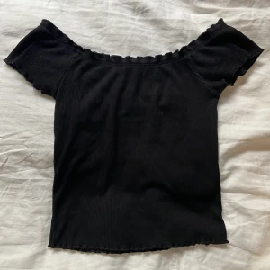 Svart topp - Svart enkel men gullig topp. Ärmarna går längs bröstet och inte över axlarna men funkar att dra upp dom om man vill då den är stretchig. Små volanger längst upp och ett fint volangmönster längst ner. Finns någon lös tråd men inget som syns eller påverkar.