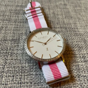 Denzel of Sweden klocka - En kanonläcker klocka från Denzel of Sweden, oanvänd, t.o.m. skyddsplasten kvar på undersidan av boetten. Vitt och rosa nato-armband. Behöver nytt batteri.
