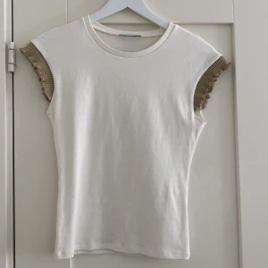 Vit t shirt  - Vit t shirt med detalj i form av guld glitter kant! Super fin, den sitter längs kroppen och inte alls oceraized. 🫶🏻 Jag leverar genom eget paket som jag tar 5 kr frakt för men väljer postnord för det finns inget annars alternativ. Så får köparen swisha!