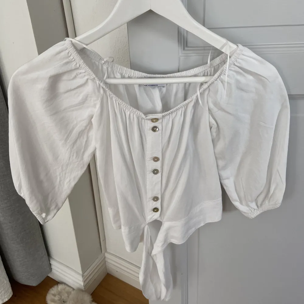 Vit blus med knappar och knytning framtill från Bershka. Kan användas både off-shoulder och vanligt. Använd fåtal gånger. 100kr + frakt. Blusar.