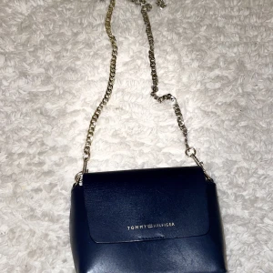 Tommy Hilfiger väska - Säljer min mörkblåa Tommy Hilfiger väska som är i fint skick och den är äkta. Det går även att ta bort kedjan som man kan se på bild 2. 