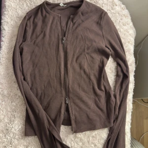 Brun topp med dragkedja  - Tröjan är från Nelly, endast använd 1 gång! Den har slits i ärmarna och dragkedja som man kan justera som man vill. 