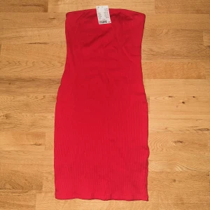 Röd klänning  - En röd bandeau klänning figursydd.  Helt oanvänd, lapp sitter kvar.