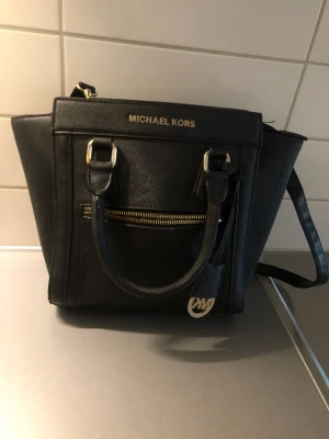 Michael Kors Väska  - Äkta Medelstor Michael Kors väska Ny pris 2500kr som kan användas både tvärs över axeln eller med handtag runt arm/i hand. Använd fåtal gånger. 